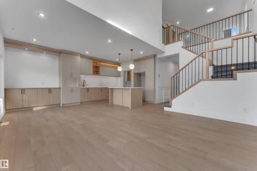 Expansive wood-finish flooring throughout, complemented by a contemporary kitchen featuring light wood-finish cabinetry, a central island, and integrated appliances - 247 Linden Loop, Leduc, AB 