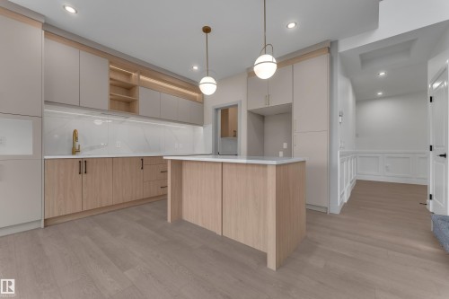 Modern kitchen featuring light wood-finish flooring, a central island with a white countertop, and integrated cabinetry - 247 Linden Loop, Leduc, AB 