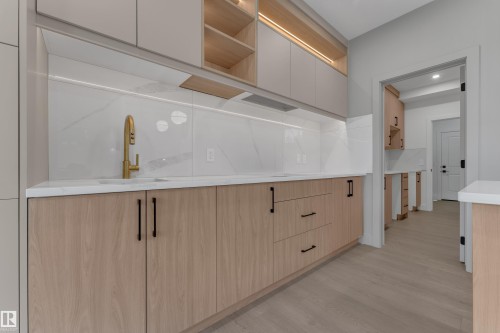 Modern kitchen featuring light wood-finish cabinetry, white stone countertops, and a white tile backsplash - 247 Linden Loop, Leduc, AB 