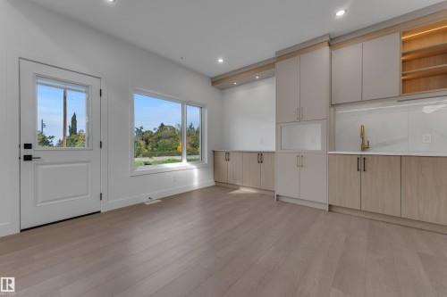 Wood-finish flooring throughout, white walls, built-in cabinetry with integrated sink and gold-tone faucet, recessed ceiling lighting, and large windows - 247 Linden Loop, Leduc, AB 