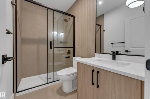 Walk-in shower with dark-framed glass enclosure, light wood-finish vanity with white countertop, integrated sink, and dark fixtures - 247 Linden Loop, Leduc, AB 