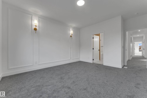 Spacious room featuring accent walls with decorative molding, wall-mounted sconces, recessed lighting, and soft gray carpeting - 247 Linden Loop, Leduc, AB 