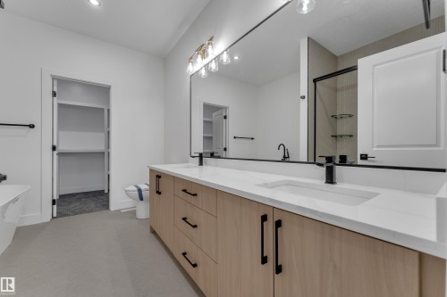 Dual vanity with light wood-finish cabinetry and matte black hardware, integrated sinks, and a large wall-mounted mirror - 247 Linden Loop, Leduc, AB 