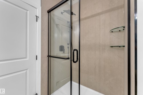 Frameless glass shower enclosure with matte black hardware, textured wall tile, and built-in glass shelves - 247 Linden Loop, Leduc, AB 