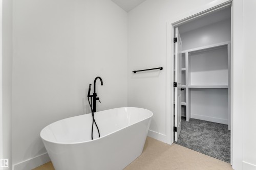 Freestanding soaking tub with matte black floor-mounted faucet, light-toned flooring, and an open closet with built-in shelving and gray carpeting - 247 Linden Loop, Leduc, AB 