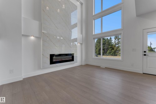 Integrated linear fireplace with a striking floor-to-ceiling tile surround, wood-finish flooring, and expansive windows - 247 Linden Loop, Leduc, AB 