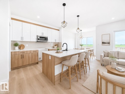 Open-concept living space with wood-finish flooring, white cabinetry, a kitchen island with seating, and large windows - 3718 67 Street, Beaumont, AB 