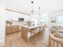 Open-concept living space with wood-finish flooring, white cabinetry, a kitchen island with seating, and large windows - 3718 67 Street, Beaumont, AB 