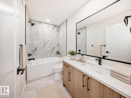 Recessed lighting, wood-finish vanity with ample storage, integrated basin, matte black fixtures, and a spacious bathtub with tiled surround - 3718 67 Street, Beaumont, AB 