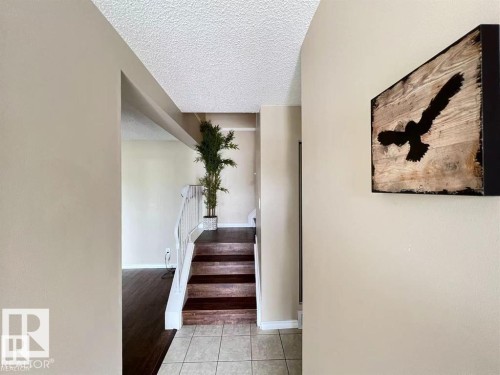 Entryway featuring tile flooring, wood-finish stairs with a white railing, and a textured ceiling - 144 Kaskitayo Court Nw, Edmonton, AB 