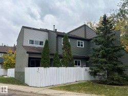 Two-story townhome with multi-toned horizontal siding, white perimeter fencing, and mature evergreen plantings - 