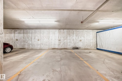 Concrete parking surface with painted yellow demarcation lines, concrete walls, and overhead fluorescent lighting - #302 4309 33 St, Stony Plain, AB 
