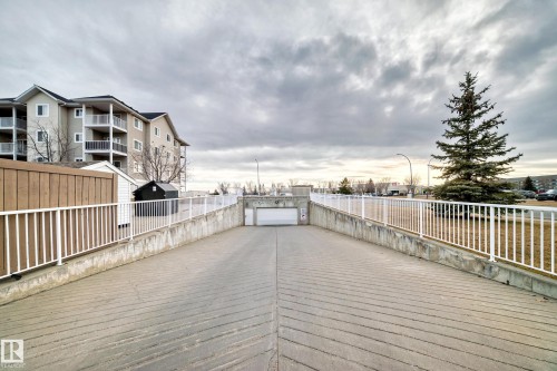 Concrete driveway ramp leading to an enclosed parking area with a garage door - #302 4309 33 St, Stony Plain, AB 