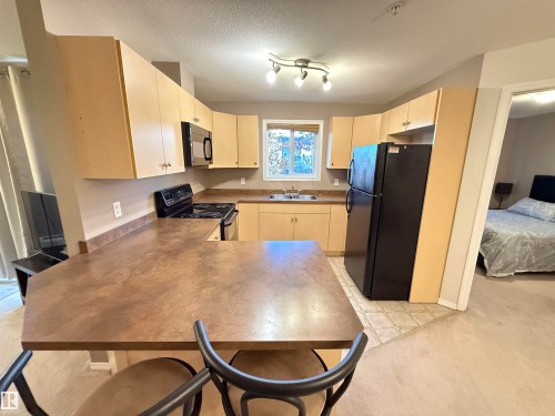 Kitchen featuring light wood-finish cabinetry, black appliances, track lighting, and a breakfast bar - #302 4309 33 St, Stony Plain, AB 