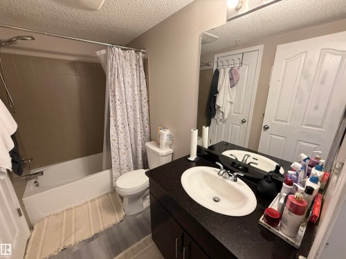 White bathtub with a chrome showerhead and faucet, tan tile surround, and a white toilet - #302 4309 33 St, Stony Plain, AB 