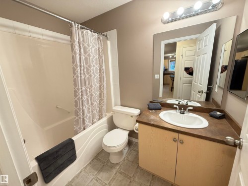 Bathtub with integrated shower, vanity with an integrated sink and countertop, wood-finish cabinetry, and tiled flooring - #302 4309 33 St, Stony Plain, AB 