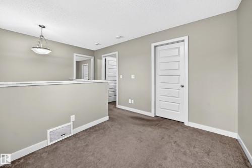 Carpeted hallway featuring a contemporary five-panel interior door, white trim, and a semi-flush mount ceiling light fixture - 1673 Cunningham Way Sw, Edmonton, AB 