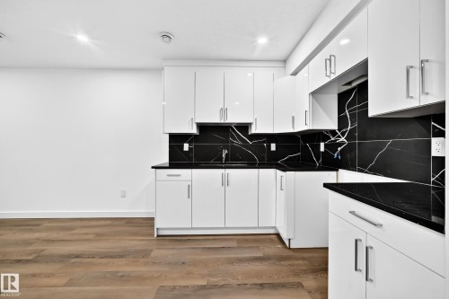 Modern kitchen featuring white cabinetry, black countertops, and a black and white patterned backsplash - 1673 Cunningham Way Sw, Edmonton, AB 