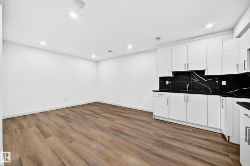 Wood-finish flooring, recessed lighting, white walls, white glossy cabinetry, and black counters with matching backsplash - 1673 Cunningham Way Sw, Edmonton, AB 