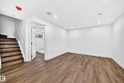 Wood-finish flooring throughout, white painted walls, recessed lighting, white trim, and a staircase with a white railing - 1673 Cunningham Way Sw, Edmonton, AB 