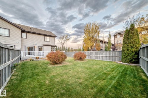 Expansive backyard featuring a manicured lawn, full perimeter fencing, and a ground-level deck with white railings - 1673 Cunningham Way Sw, Edmonton, AB 
