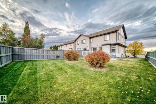 Fenced backyard with a manicured lawn, two mature shrubs, and a white deck - 1673 Cunningham Way Sw, Edmonton, AB 