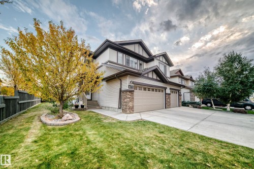 Exterior featuring a concrete driveway, attached two-car garage, stone and siding accents, and a landscaped front yard with mature trees - 1673 Cunningham Way Sw, Edmonton, AB 