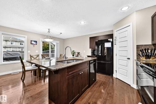 Hardwood-finish flooring, recessed lighting, island with integrated sink, stone countertop, and dark wood cabinetry - 1673 Cunningham Way Sw, Edmonton, AB 