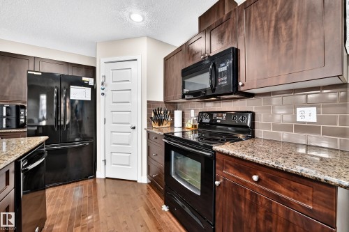 Kitchen featuring wood-finish flooring, dark wood cabinetry, black appliances, granite countertops, and subway tile backsplash - 1673 Cunningham Way Sw, Edmonton, AB 