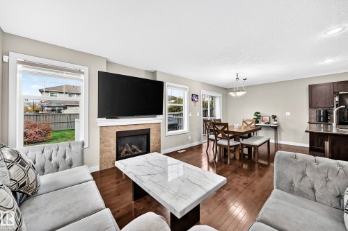 Hardwood-finish flooring, built-in fireplace with stone-tile surround, multiple windows with white trim, recessed lighting, and a sliding glass door - 1673 Cunningham Way Sw, Edmonton, AB 