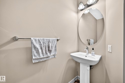 Pedestal sink with a polished chrome faucet, oval mirror, and wall-mounted vanity lighting - 1673 Cunningham Way Sw, Edmonton, AB 