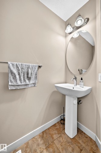Pedestal sink with chrome faucet, oval mirror, and a two-light vanity fixture - 1673 Cunningham Way Sw, Edmonton, AB 