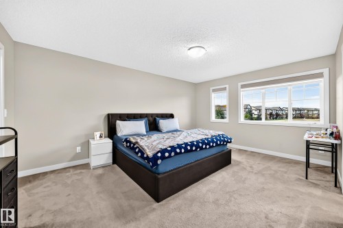 Expansive room with neutral tone walls, textured ceiling, flush mount lighting, and large windows with white trim - 1673 Cunningham Way Sw, Edmonton, AB 
