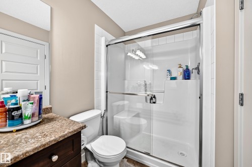 Shower enclosure with sliding glass door, white toilet, and dark wood-finish vanity with a brown countertop - 1673 Cunningham Way Sw, Edmonton, AB 