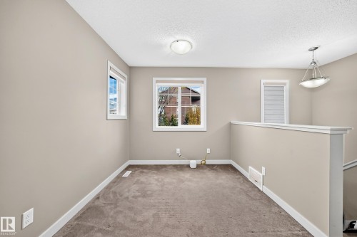 Neutral-toned walls, recessed lighting, window with exterior landscape, carpeted flooring, and a contemporary pendant light fixture - 1673 Cunningham Way Sw, Edmonton, AB 