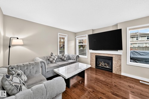 Hardwood flooring, light-toned walls, multiple windows, and a built-in fireplace with a stone surround - 1673 Cunningham Way Sw, Edmonton, AB 