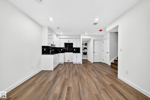 Wood-finish flooring throughout, kitchen with white cabinetry, black countertops, and black tile backsplash - 1673 Cunningham Way Sw, Edmonton, AB 