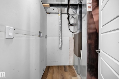 Wood-finish flooring with unfinished drywall, white paneled door, and exposed utility components - 1673 Cunningham Way Sw, Edmonton, AB 