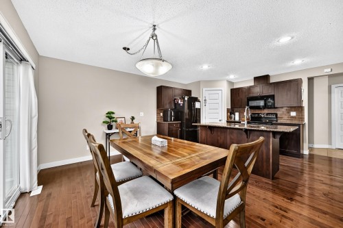 Wood-finish flooring, sliding glass door, recessed lighting, pendant light fixture, and dark wood-finish cabinetry - 1673 Cunningham Way Sw, Edmonton, AB 