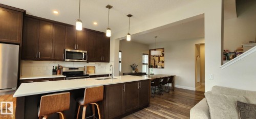Gourmet kitchen featuring dark wood cabinetry, stainless steel appliances, a center island with seating, pendant lighting, and wood-finish flooring - 3779 Cherry Loop Sw, Edmonton, AB 