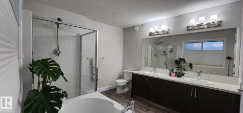 Glass-enclosed shower, built-in bathtub, double vanity with dual sinks, wood-finish flooring, and a large mirror - 3779 Cherry Loop Sw, Edmonton, AB 