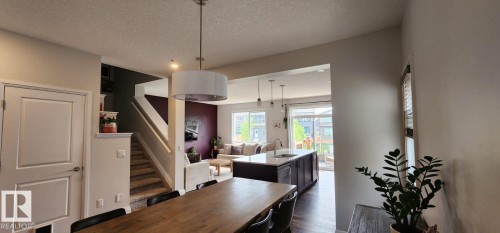 Open-concept living area featuring a kitchen island with seating, dark wood-finish flooring, and a contemporary ceiling light fixture - 3779 Cherry Loop Sw, Edmonton, AB 