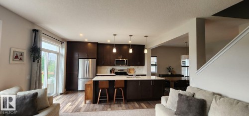 Kitchen featuring dark wood cabinetry, stainless steel appliances, a center island with pendant lighting, and wood-finish flooring - 3779 Cherry Loop Sw, Edmonton, AB 