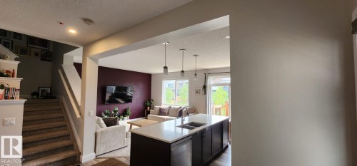 Open-concept living space featuring a kitchen island with sink, pendant lighting, and wood-finish flooring - 3779 Cherry Loop Sw, Edmonton, AB 