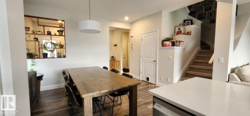 Wood-finish flooring throughout, featuring a drum pendant light fixture, built-in wall shelving, and a carpeted staircase with a white railing - 3779 Cherry Loop Sw, Edmonton, AB 