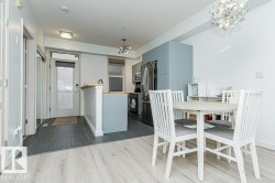 Open-concept living area with wood-finish flooring, a kitchen island with a wood-finish countertop, stainless steel appliances, and a modern light fixture - 