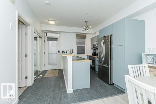 Modern kitchen featuring light blue cabinetry, stainless steel appliances, and a breakfast bar - #202 9503 101 Av Nw, Edmonton, AB 