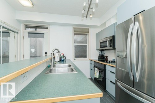 Kitchen with green countertops, stainless steel double-basin sink, stainless steel refrigerator, stainless steel microwave, and track lighting - #202 9503 101 Av Nw, Edmonton, AB 
