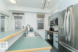 Kitchen with green countertops, stainless steel double-basin sink, stainless steel refrigerator, stainless steel microwave, and track lighting - 