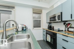 Stainless steel double basin sink with a high-arc faucet, light blue flat-panel cabinetry, wood-finish countertops, stainless steel microwave, and integrated cooktop - 
